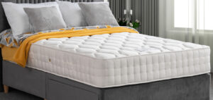 Apley Natural Augusta 1000 Pocket Sprung Mattress with white quilted fabric, placed on a grey upholstered bed frame, with grey and yellow bedding.