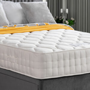 Apley Natural Augusta 1000 Pocket Sprung Mattress with white quilted fabric, placed on a grey upholstered bed frame, with grey and yellow bedding.