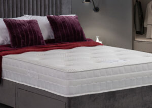 Olivia Memory Mattress with a soft knitted fabric and 3D mesh border, displayed on a bed with rich burgundy pillows and a textured throw.