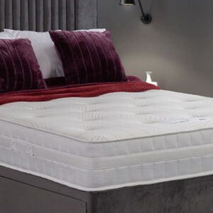 Olivia Memory Mattress with a soft knitted fabric and 3D mesh border, displayed on a bed with rich burgundy pillows and a textured throw.