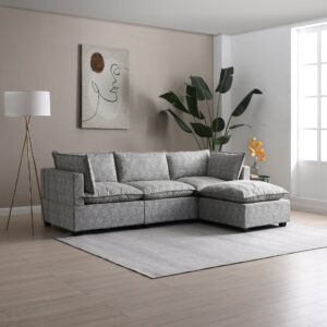 A stylish and modern Kyoto Moda corner sofa with a chaise, upholstered in a textured grey bouclé fabric, set in a neutrally toned living room. The room is tastefully decorated with a minimalist abstract canvas painting, a sleek tripod floor lamp with a white shade, and a vibrant tropical plant in a corner. A subtle grey rug under the sofa adds to the room's contemporary charm, while natural light from a nearby window creates an inviting atmosphere. The scene is accented with a small side table displaying a vase of orange flowers, contributing a pop of color to the serene palette.