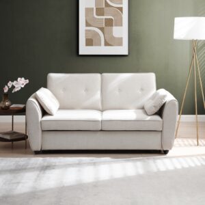 A cream-colored Kyoto Willow sofa bed placed in a bright, modern living room setting with a side table, lamp, and decorative art piece in the background.