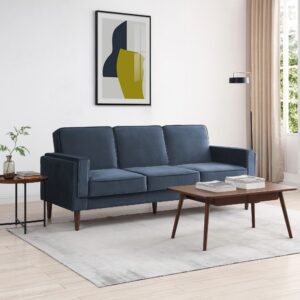 A stylish Paolo sofa bed in ink velvet displayed in a modern living room with a coffee table and decorative art on the wall.