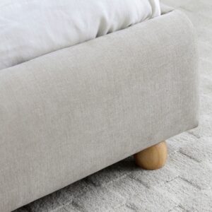 Detail of the Mollie bed's natural upholstered base and wooden ball foot on a cream rug