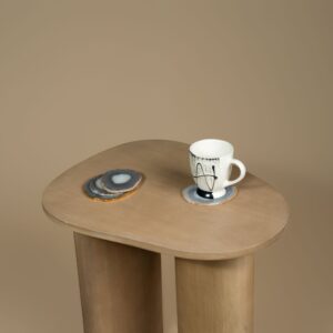 Sutton Lamp Table styled with a mug and coaster, showing the rounded mango wood top and wide oval legs