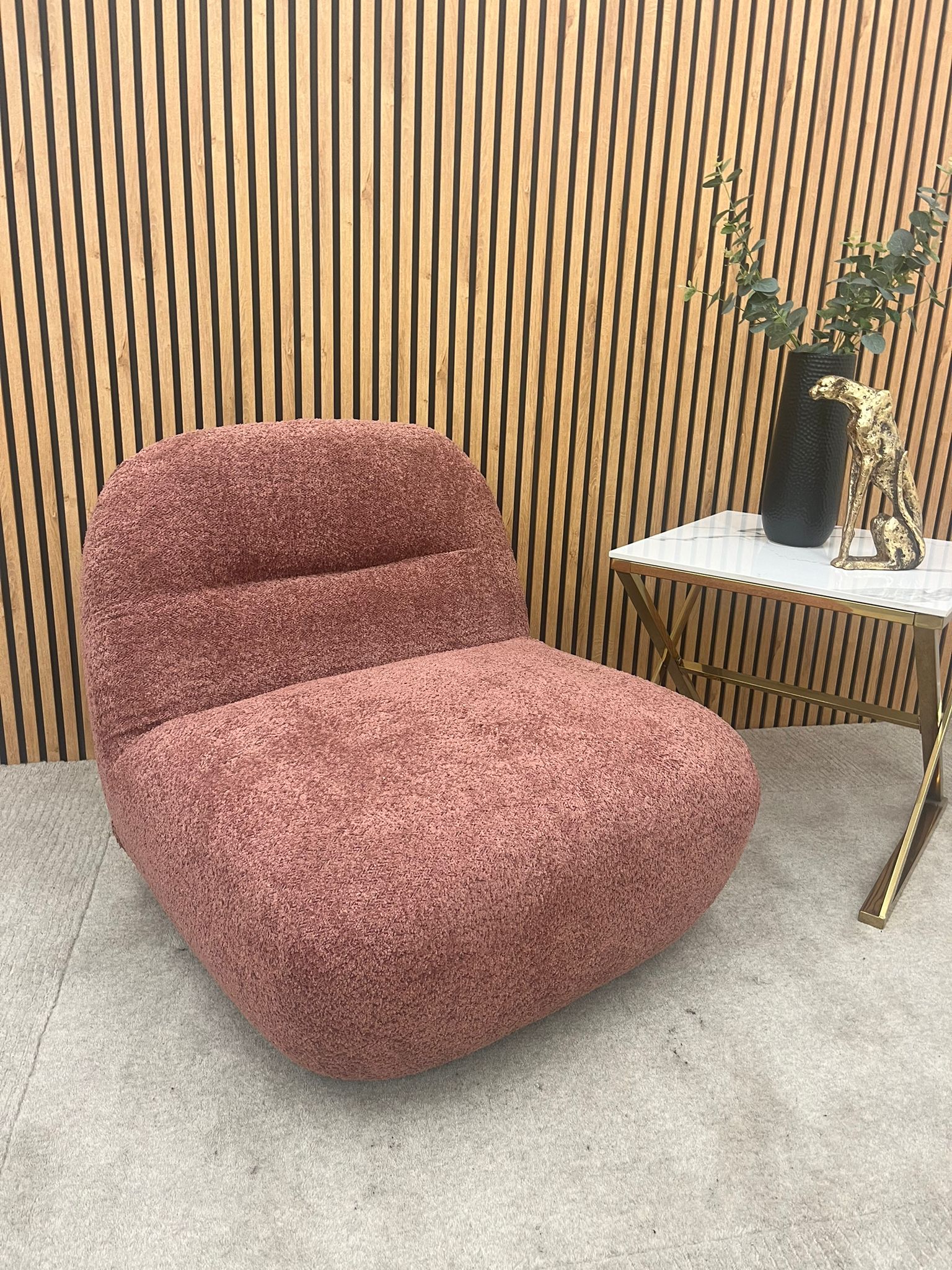 Miami swivel accent chair in blush orange boucle styled in a room with slatted wood panelling and a side table
