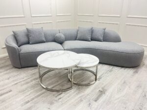 Pebble grey boucle curved sofa styled in a panelled living room with marble nesting coffee tables
