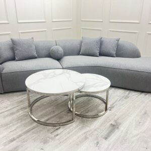 Pebble grey boucle curved sofa styled in a panelled living room with marble nesting coffee tables