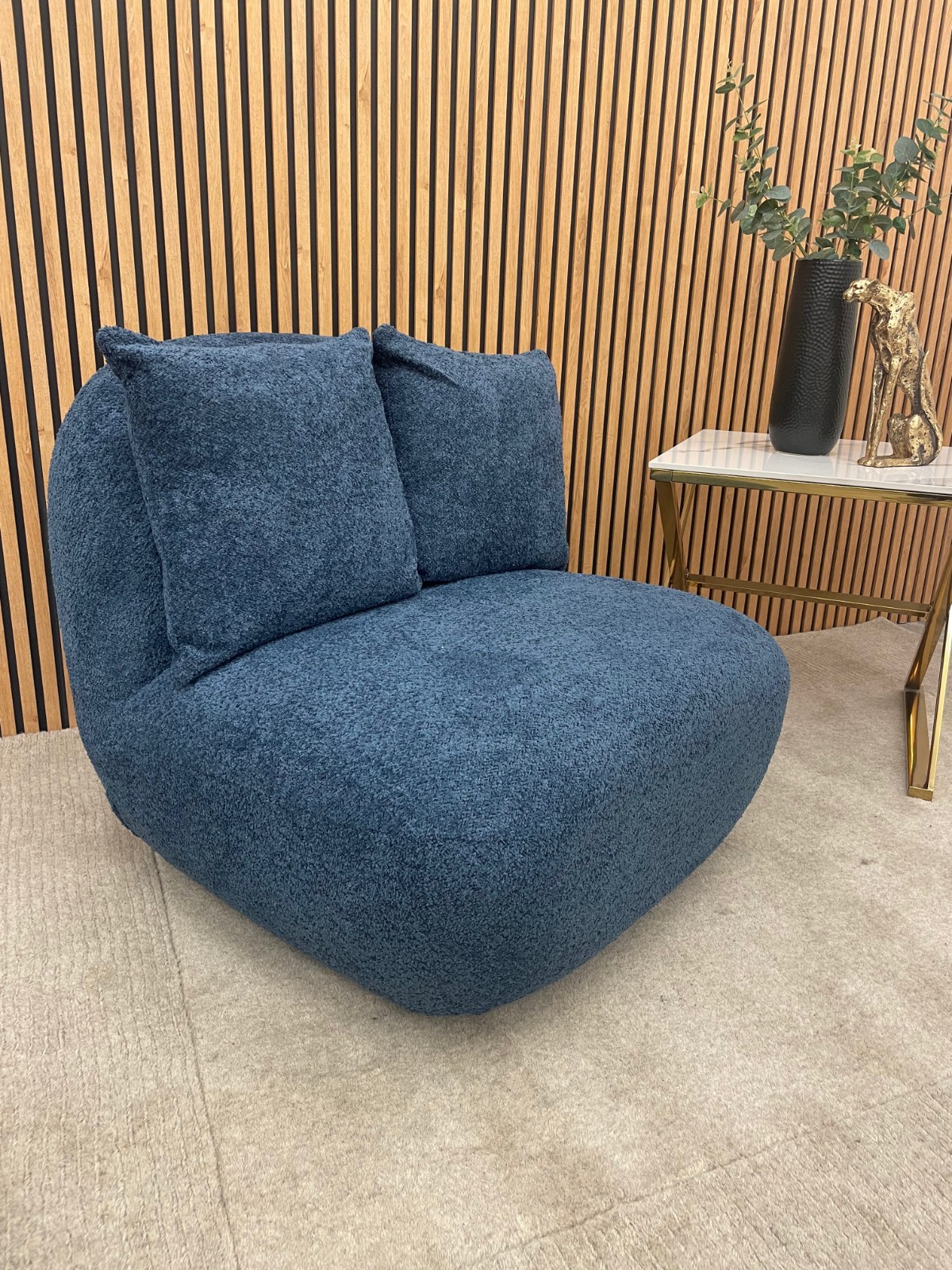 Miami swivel accent chair in navy blue boucle with two scatter cushions against slatted wood panelling