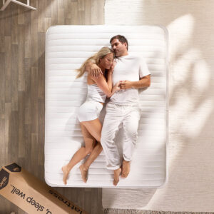 Overhead view of a couple lying on the Jay-Be Pure Anti-Allergy mattress beside its delivery box