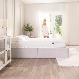 Woman by the window with the Pure Anti-Allergy sprung mattress on a white divan base in a bright bedroom
