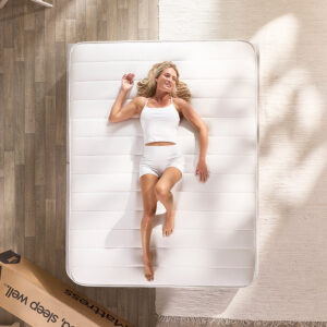 Overhead view of a woman lying on the Pure Anti-Allergy sprung mattress beside its delivery box on a wooden floor