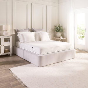 Jay-Be Pure Anti-Allergy Comfort Sprung mattress on a white divan in a light bedroom with a bedside cabinet and rug