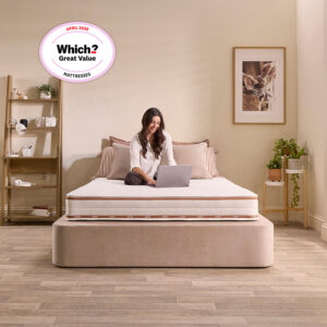 Woman sitting cross-legged on the Jay-Be Ryze Deep Quilted mattress with a laptop in a neutral bedroom