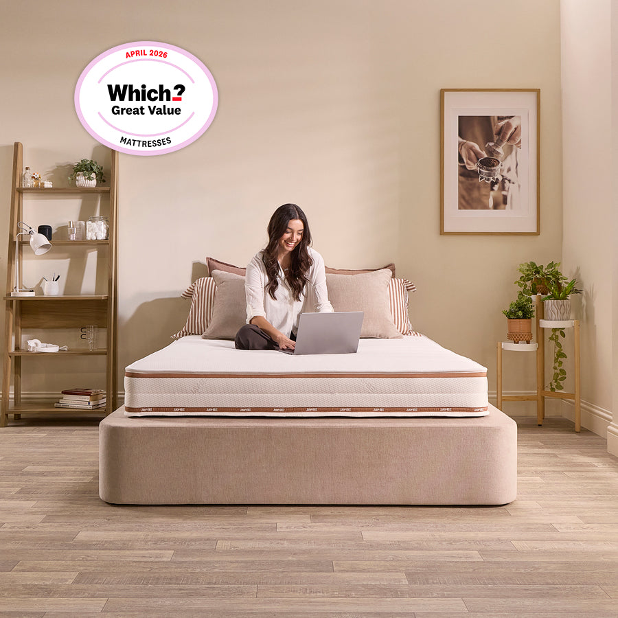 Woman sitting cross-legged on the Jay-Be Ryze Deep Quilted mattress with a laptop in a neutral bedroom