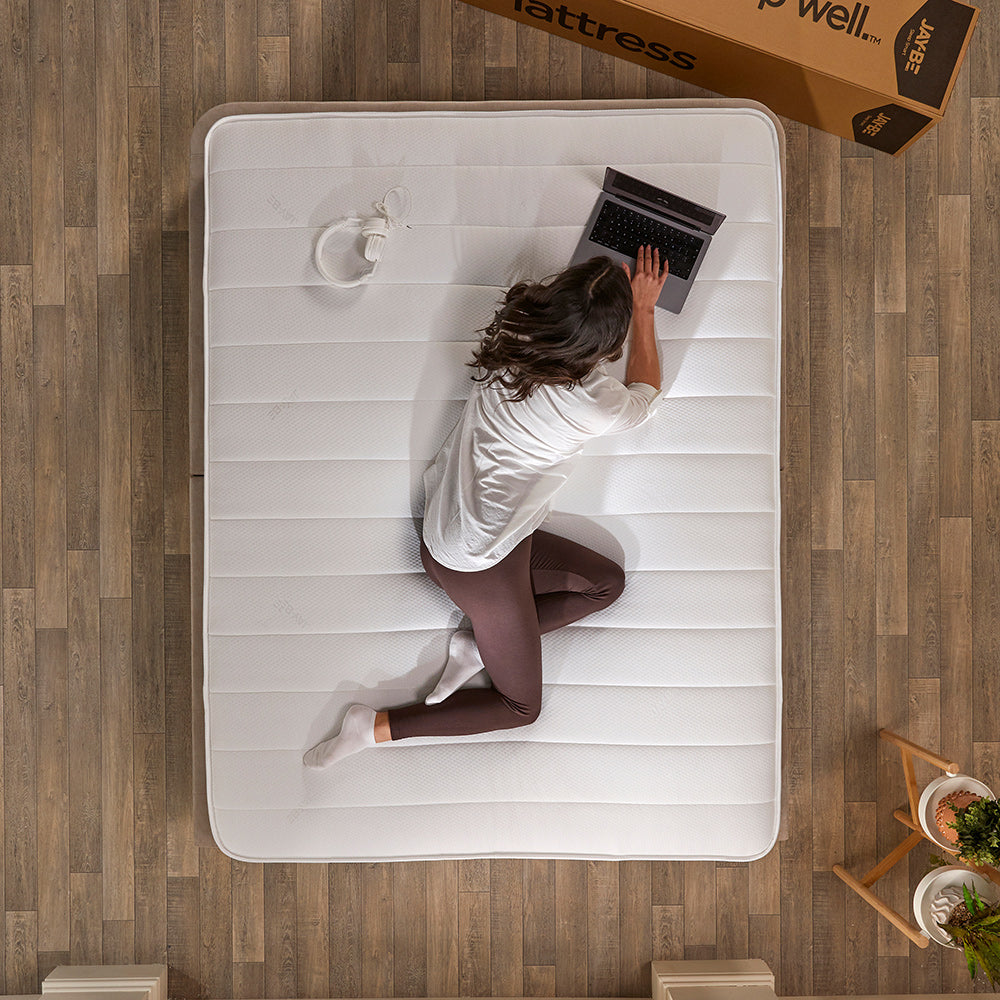 Overhead view of a woman lying on the Ryze Deep Quilted mattress beside its delivery box on a wooden floor