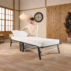 Man making up the Jay-Be Tourist folding bed with a pillow in a guest room