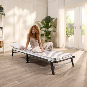 Woman sitting on the Jay-Be ME70 Mobile folding bed with a pillow, showing it takes an adult